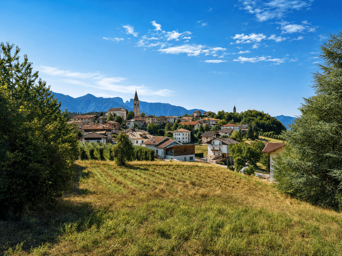 Malerisches Dorf mit Kirchturm, umgeben von grünen Feldern und majestätischen Bergen.
