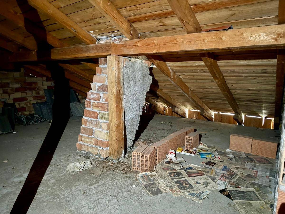 Unausgebauter Dachboden mit sichtbaren Holzbalken und Ziegelwänden, bietet viel Stauraum.