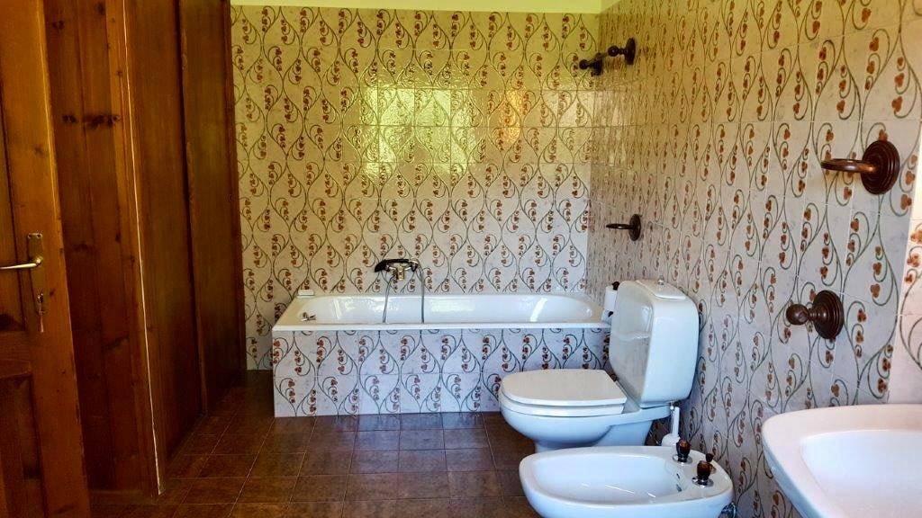 Badezimmer mit Badewanne, Toilette und Bidet, charakterisiert durch gemusterte Fliesen im Stil der 80er Jahre.