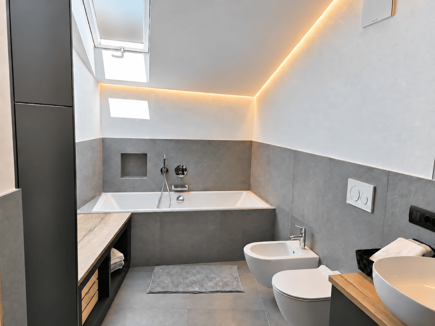 Modernes Badezimmer mit Badewanne, Bidet, WC und einem Dachfenster für natürliches Licht.
