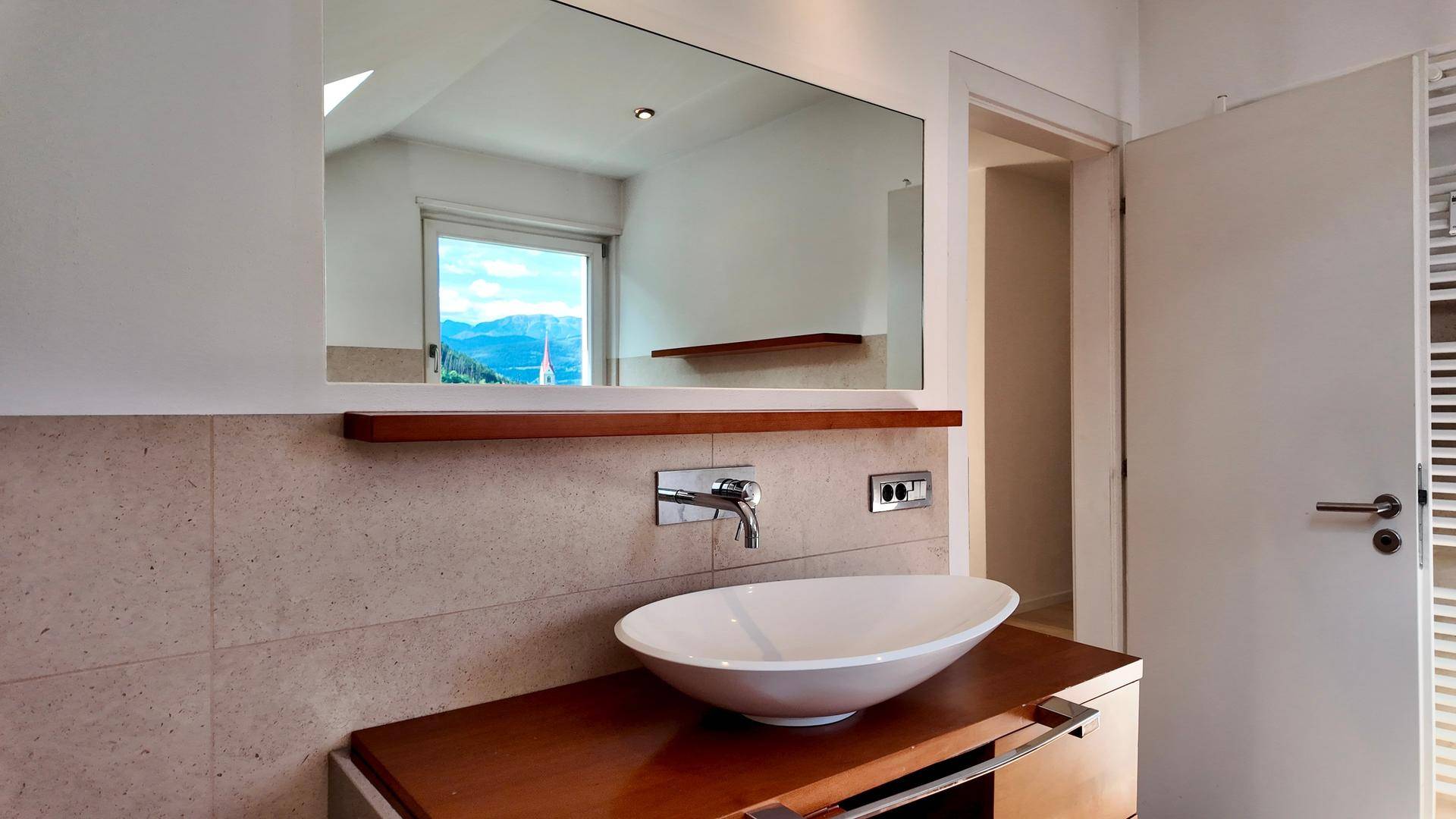Modernes Badezimmer mit ovalem Aufsatzwaschbecken, großem Spiegel und Holzablage.