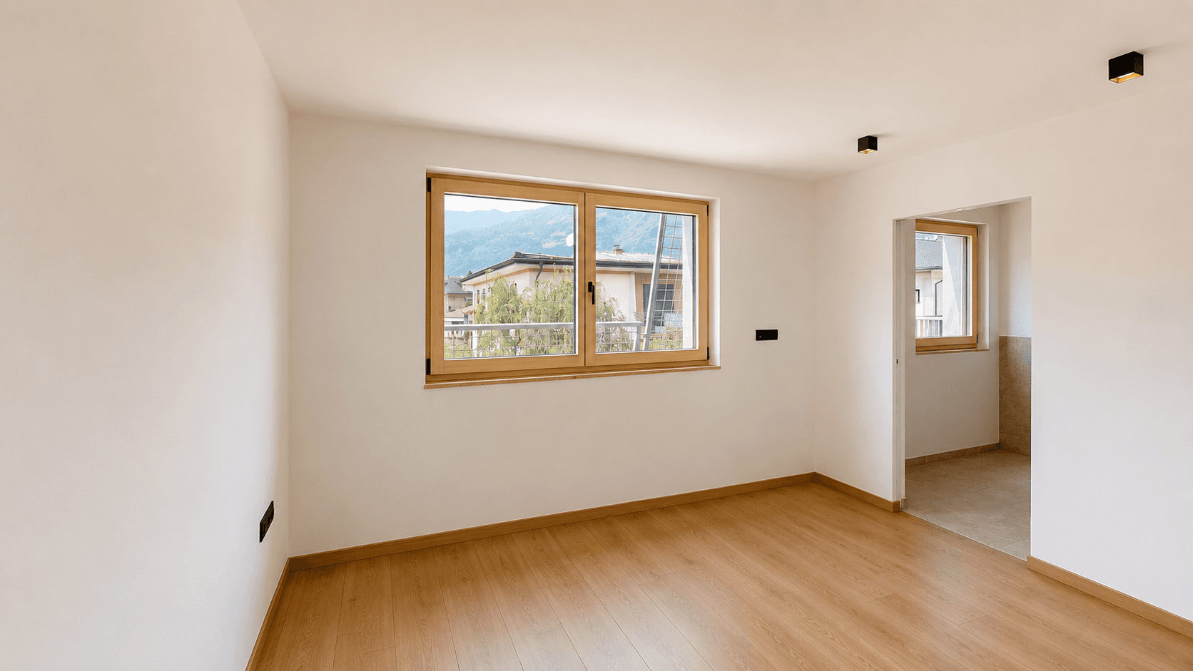 Helles Zimmer mit Holzboden und Bergblick, das in einen gefliesten Bereich führt.