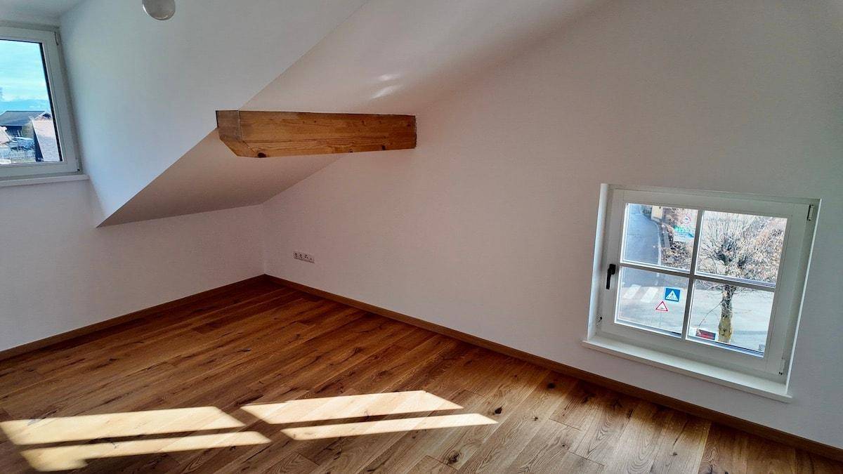 Geräumiges Dachgeschosszimmer mit Holzboden, schrägen Wänden und zwei Fenstern.
