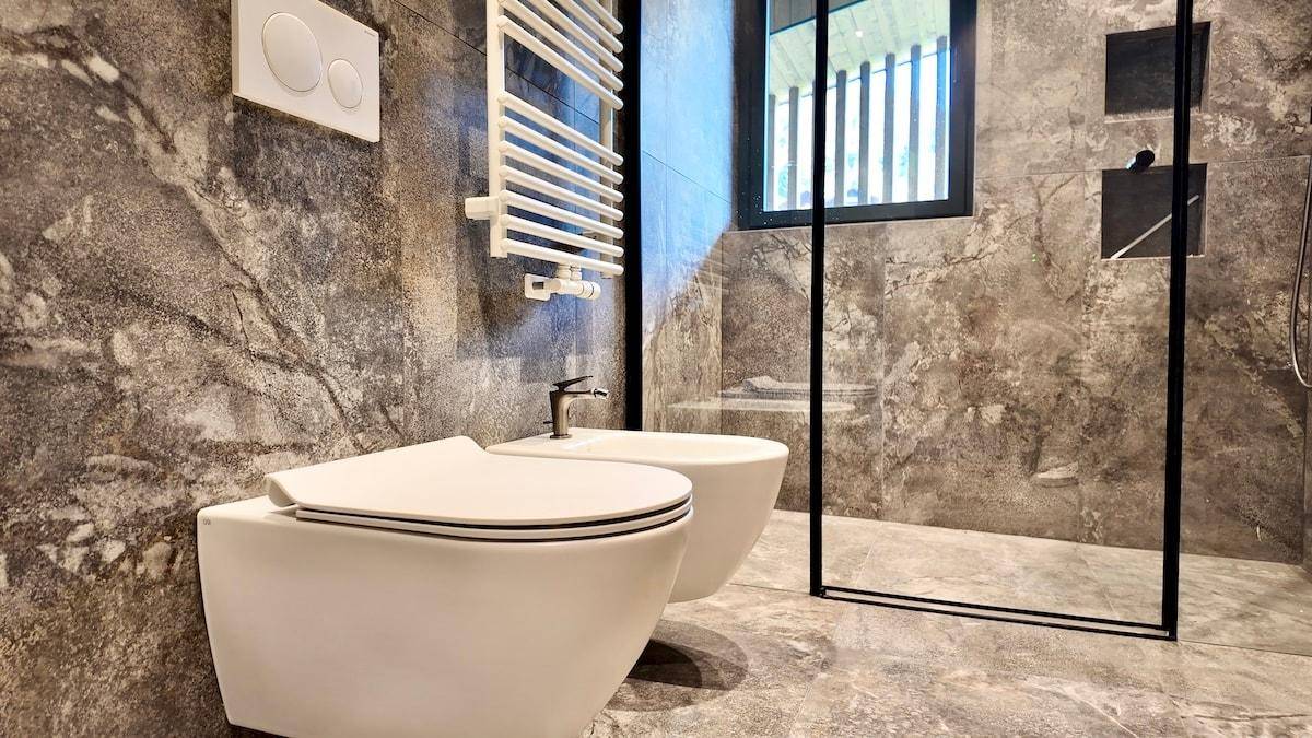 Modernes Badezimmer mit großformatigen Fliesen, wandhängendem WC, Bidet und beheiztem Handtuchhalter.