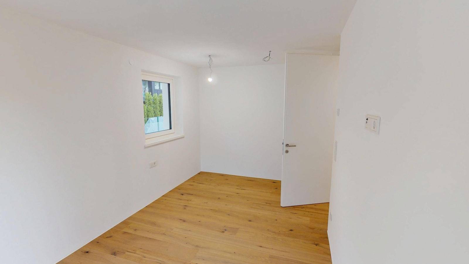 Helles Schlafzimmer mit Holzboden und einem Fenster, das viel Tageslicht hereinlässt.