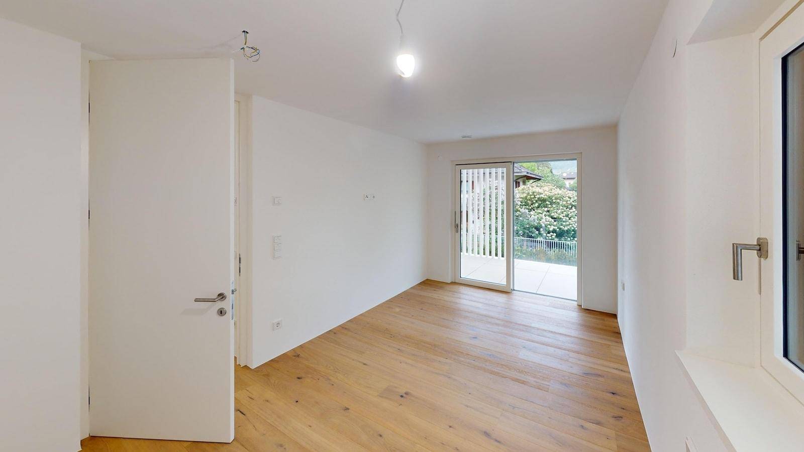 Helles, unmöbliertes Zimmer mit Holzboden und Zugang zu einem Außenbereich mit Terrasse.