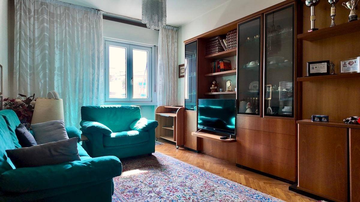 Wohnzimmer mit großem Holzschrank, türkisfarbenem Sofa und Teppichboden.