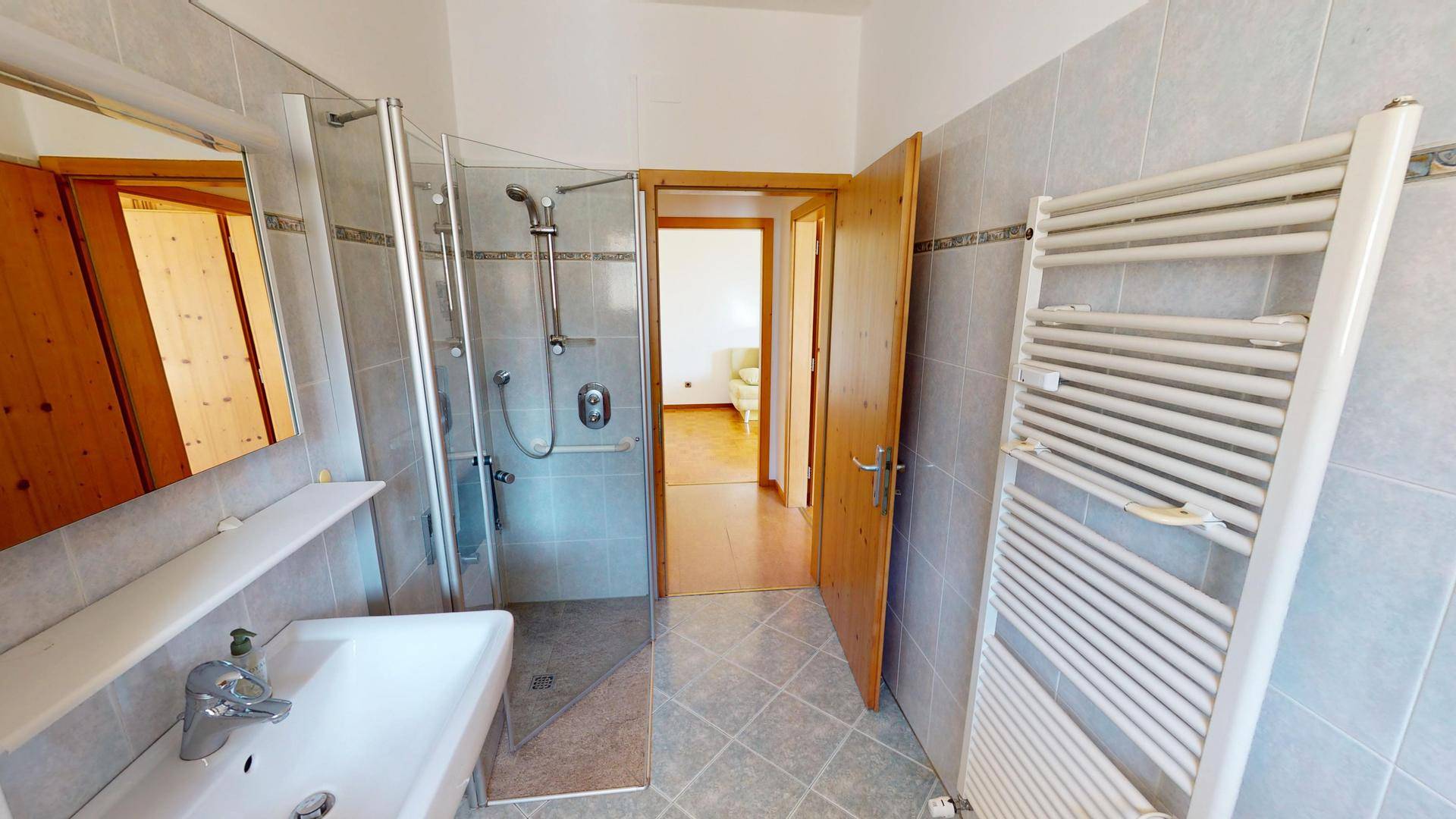 Badezimmer mit Duschkabine, Waschbecken und beheiztem Handtuchhalter.
