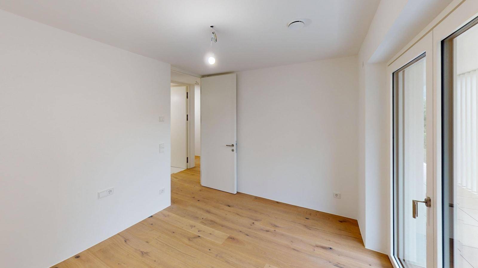 Unmöblierter Raum mit Holzboden und Zugang zu einem Balkon oder einer Terrasse.