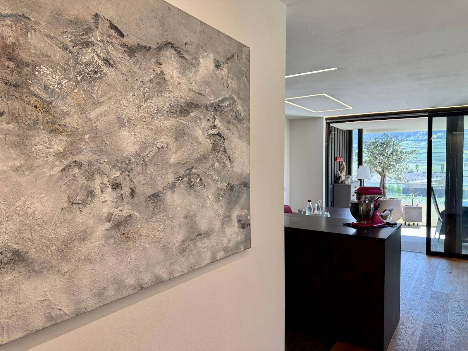 Abstrakte Kunst an der Wand, die einen Einblick in den hellen Wohnbereich und die Terrasse gewährt.