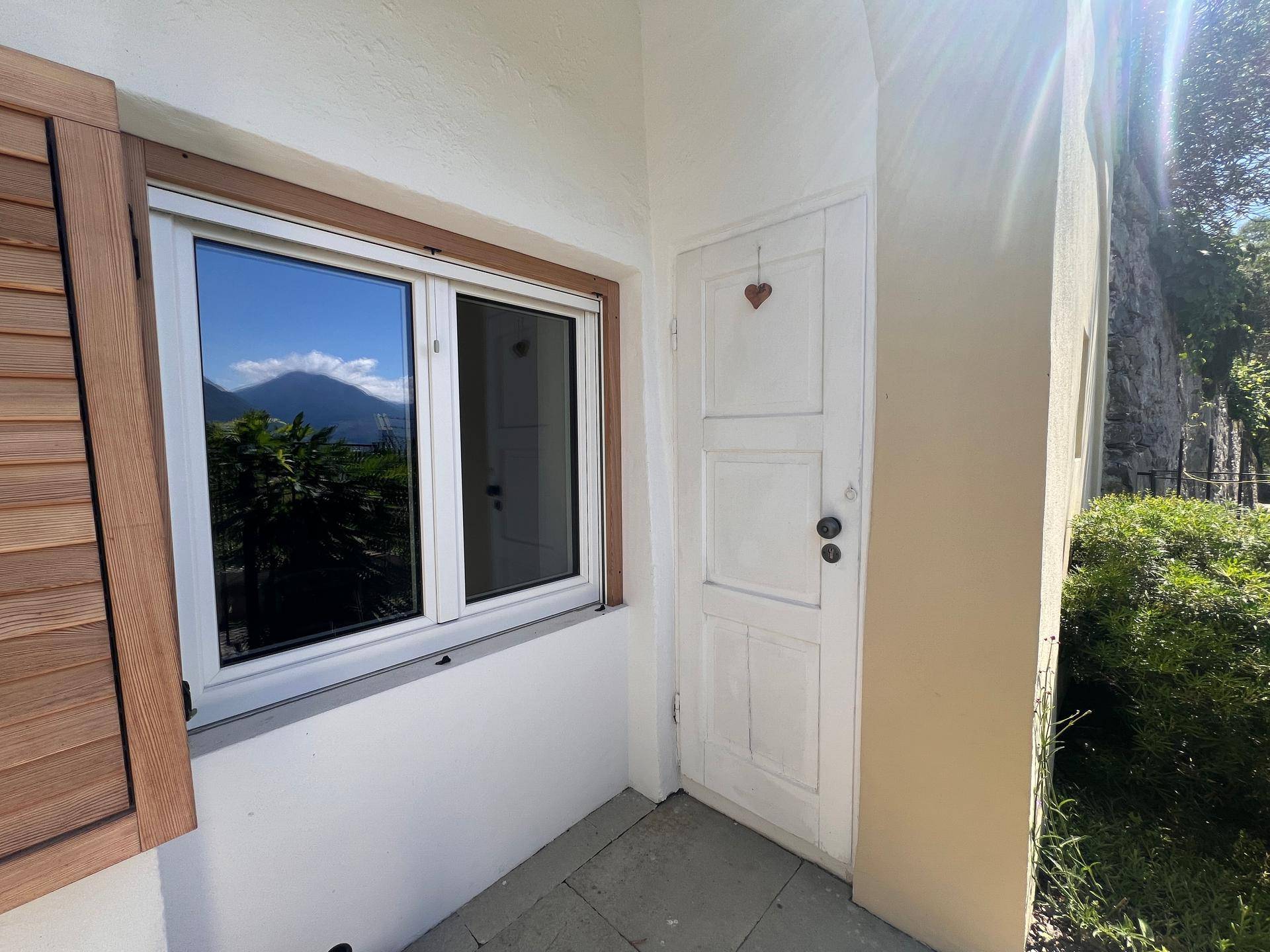 Eingangsbereich mit weißer Tür und Fenster, das einen klaren Bergblick widerspiegelt.
