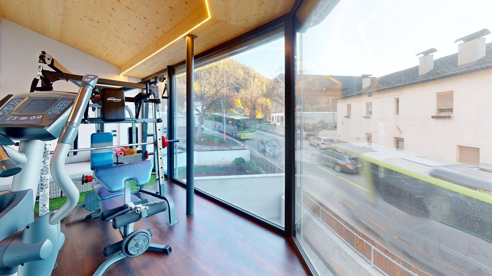 Fitnessbereich mit großen Panoramafenstern und Blick auf die Straße und umliegende Gebäude.