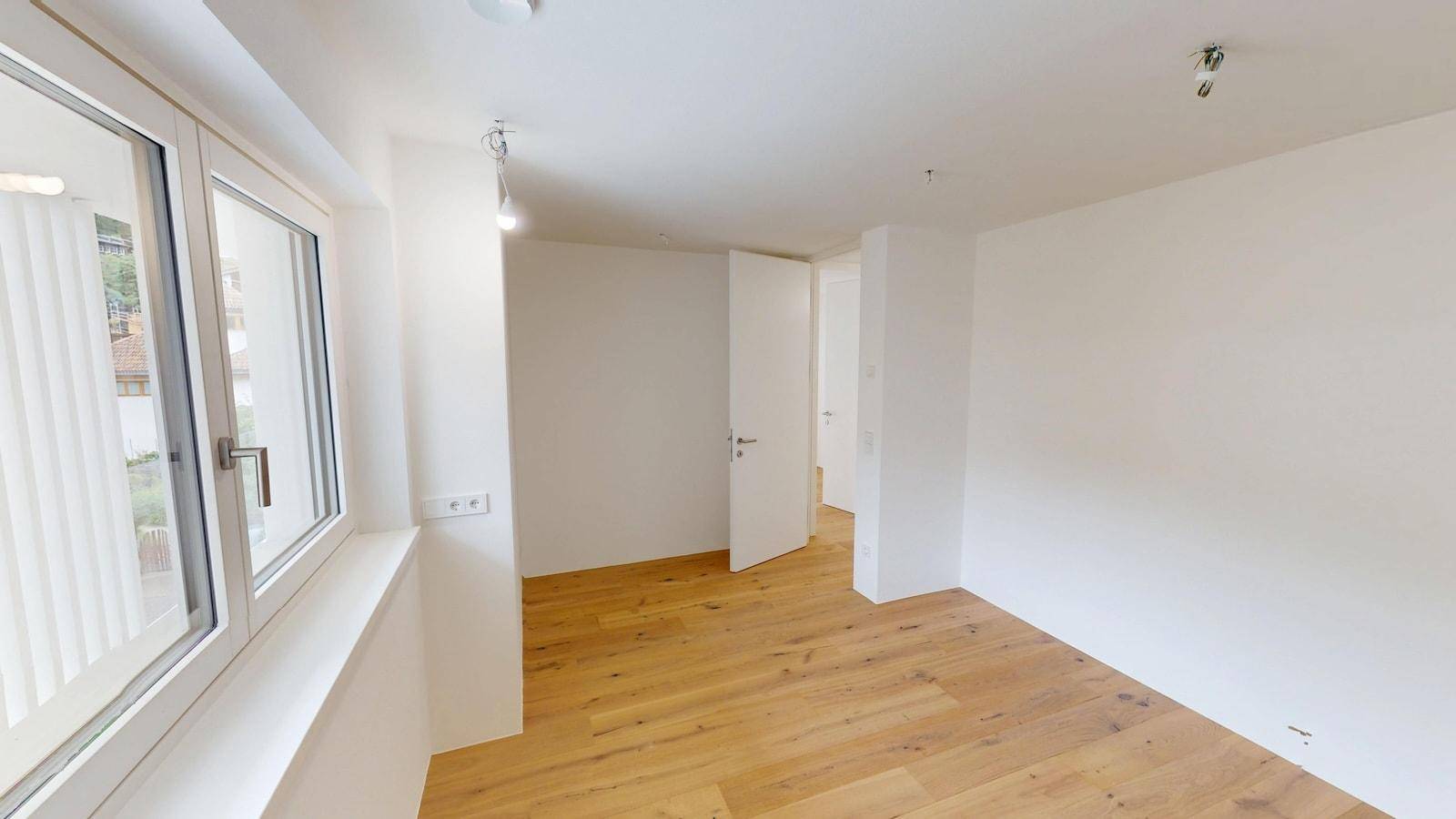 Helles Zimmer mit Parkettboden und einem großen Fenster, das den Raum mit Tageslicht füllt.