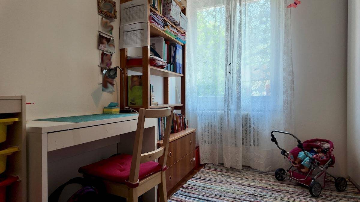 Helles Kinderzimmer mit Schreibtisch, Bücherregal und Fenster mit Vorhängen, ideal zum Lernen.