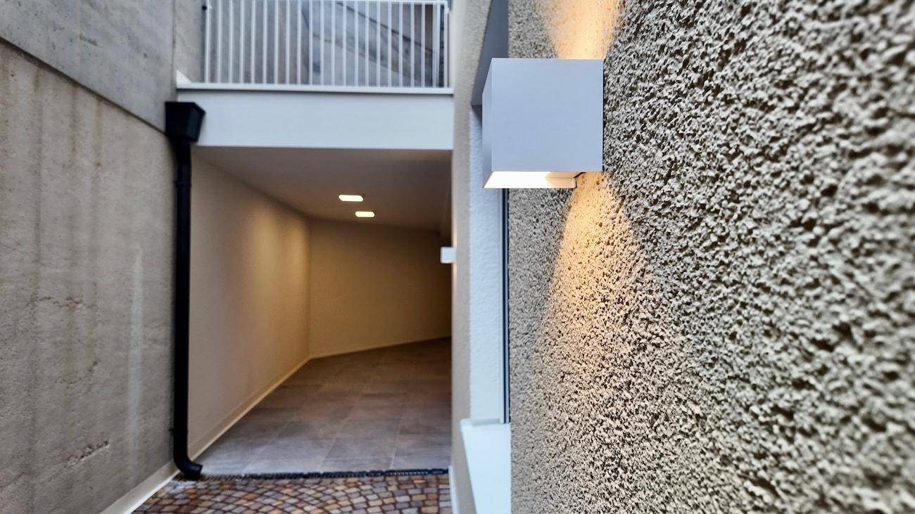 Detailansicht einer strukturierten Außenwand mit moderner Beleuchtung und einem Durchgang.