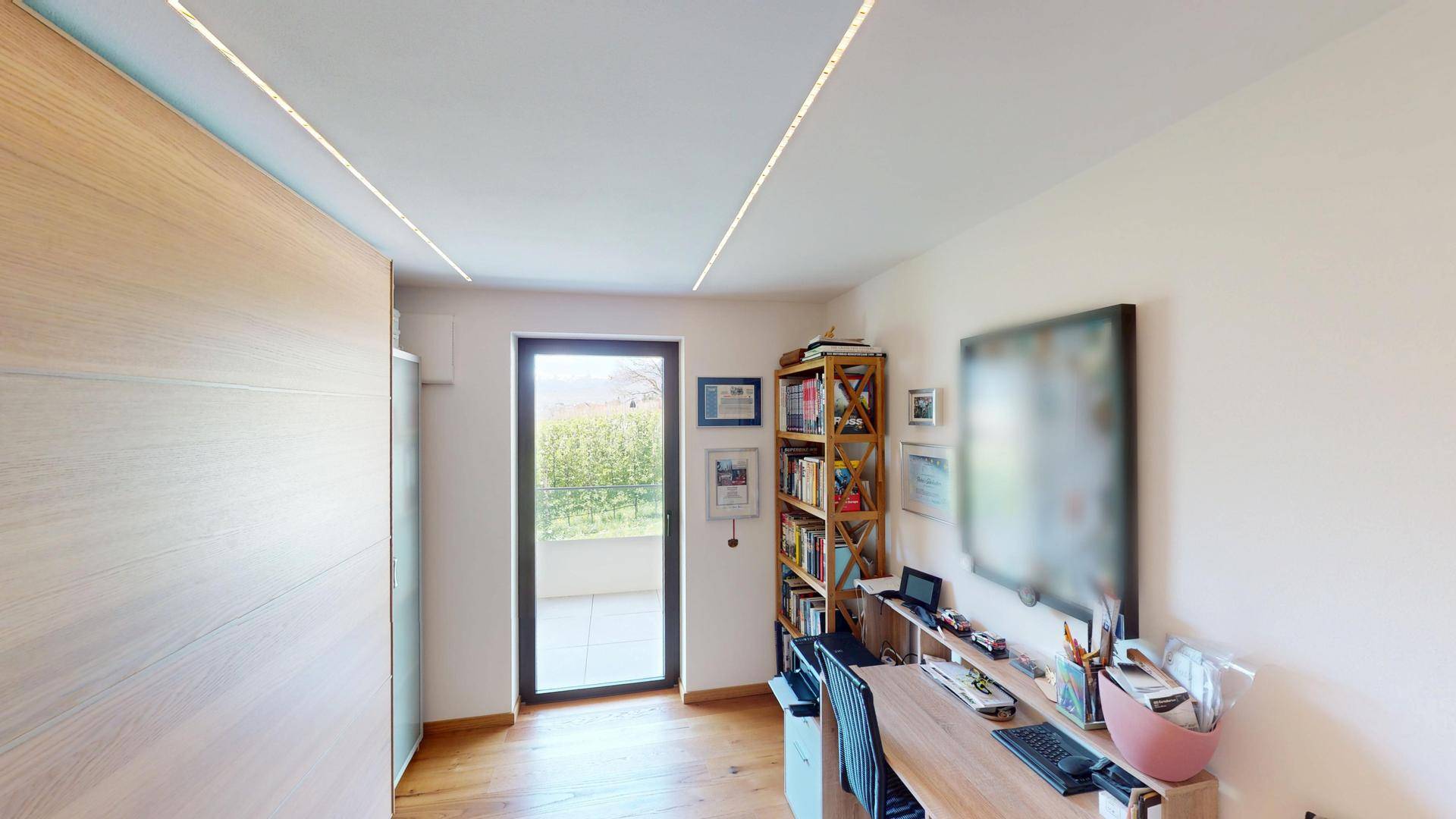 Arbeitszimmer mit Holzboden, Bücherregal und Tür, die zu einem Außenbereich führt.