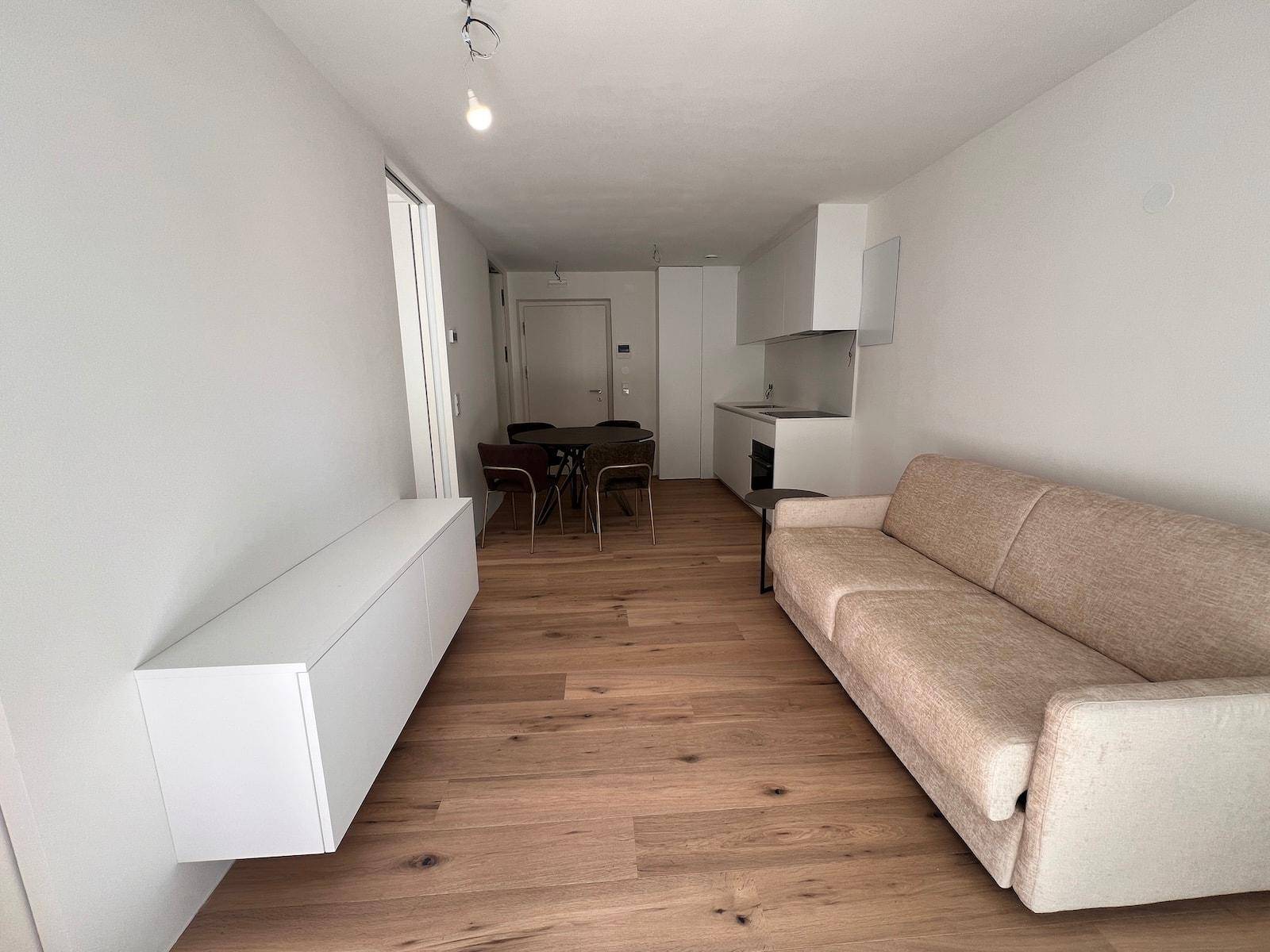 Heller Wohnbereich mit beigem Sofa, schwebendem Sideboard und Holzboden in offener Gestaltung.