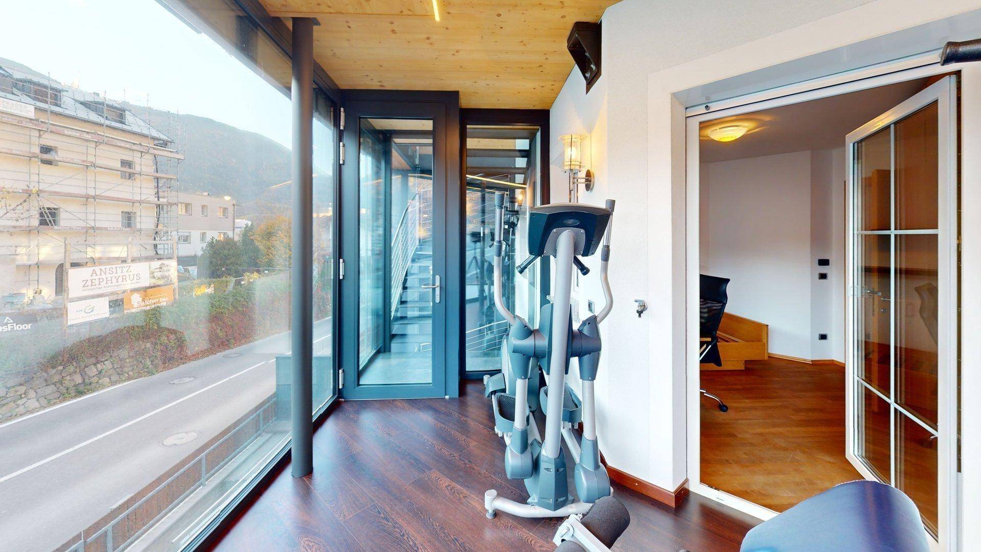 Heller Fitnessraum mit Trainingsgeräten und raumhohen Fenstern, die einen weiten Blick bieten.