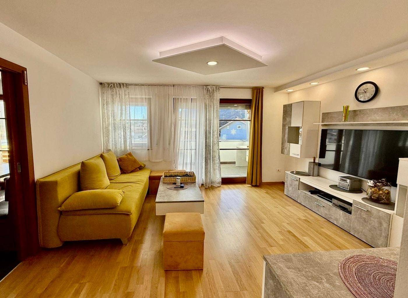 Helles Wohnzimmer mit Parkettboden, gelbem Sofa und modernem TV-Möbel.