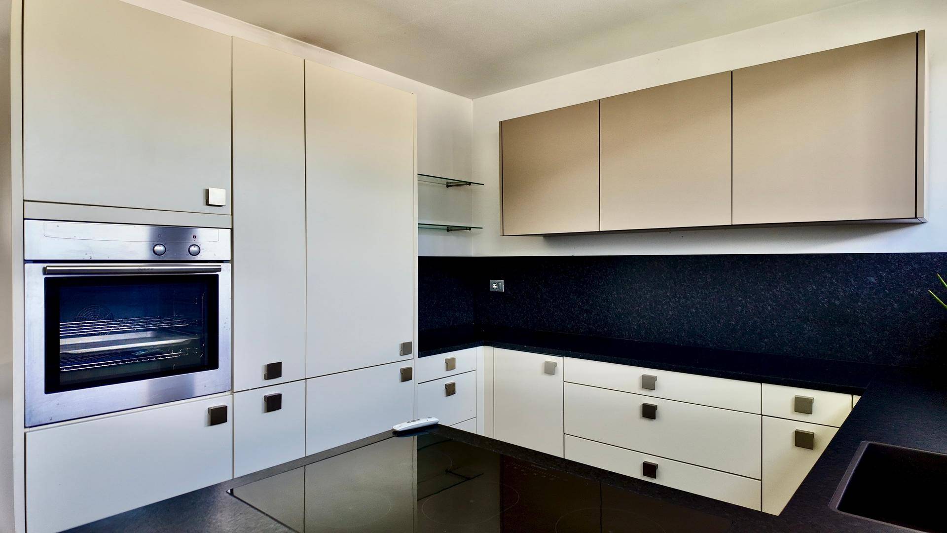 Einbauküche mit modernem Backofen, weißen Schränken und dunkler Arbeitsfläche.