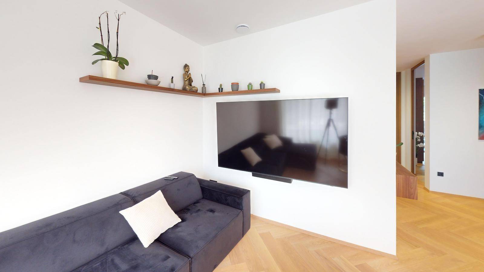 Wohnzimmer mit großem Sofa, Wandfernseher und dekorativen Regalen.