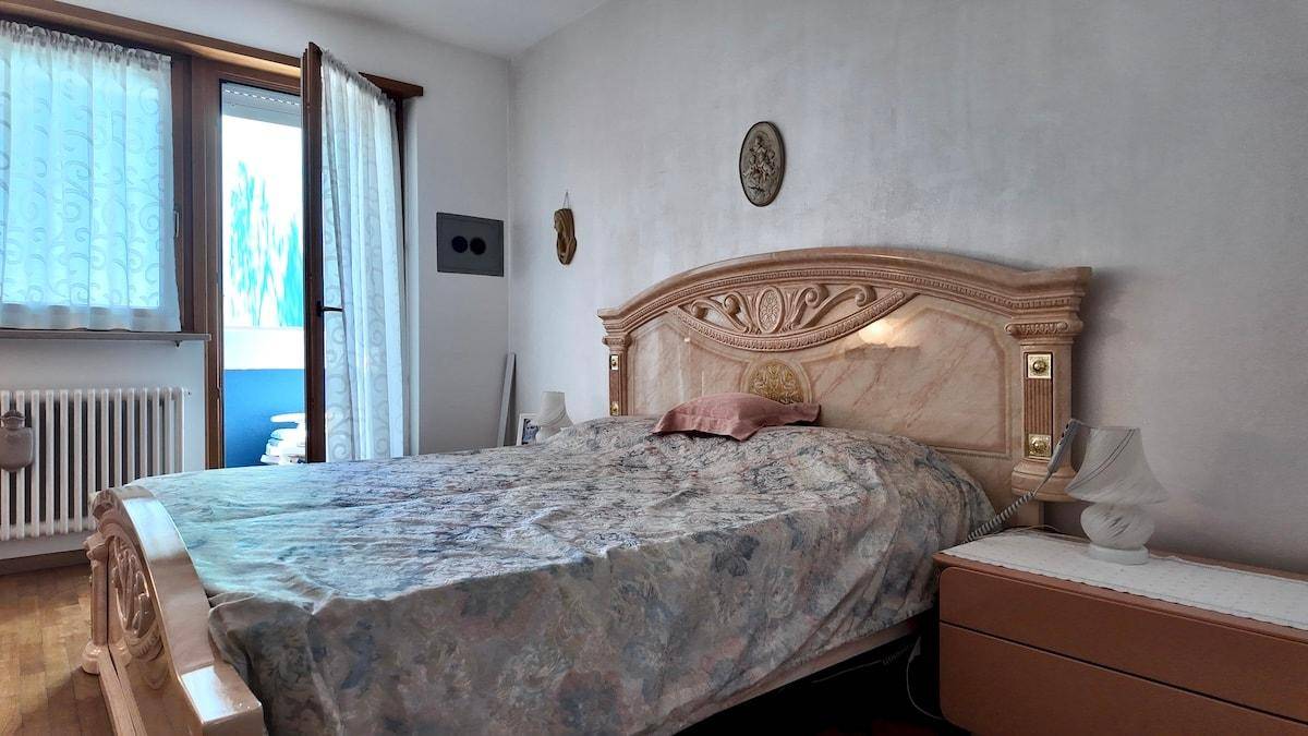 Schlafzimmer mit großem Bett, geschnitztem Kopfteil und Zugang zum Balkon.