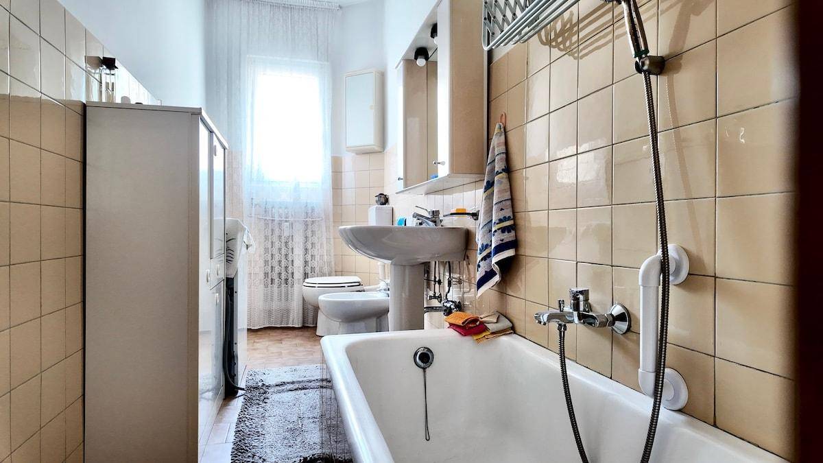 Badezimmer mit Badewanne, Waschbecken und beigen Fliesen an den Wänden.