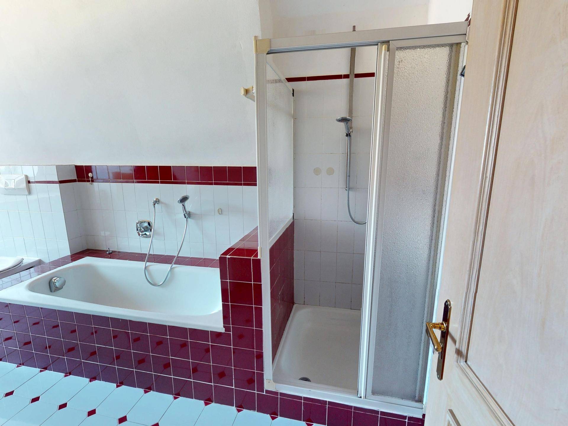Badezimmer mit Badewanne, Dusche und roten Akzentfliesen.