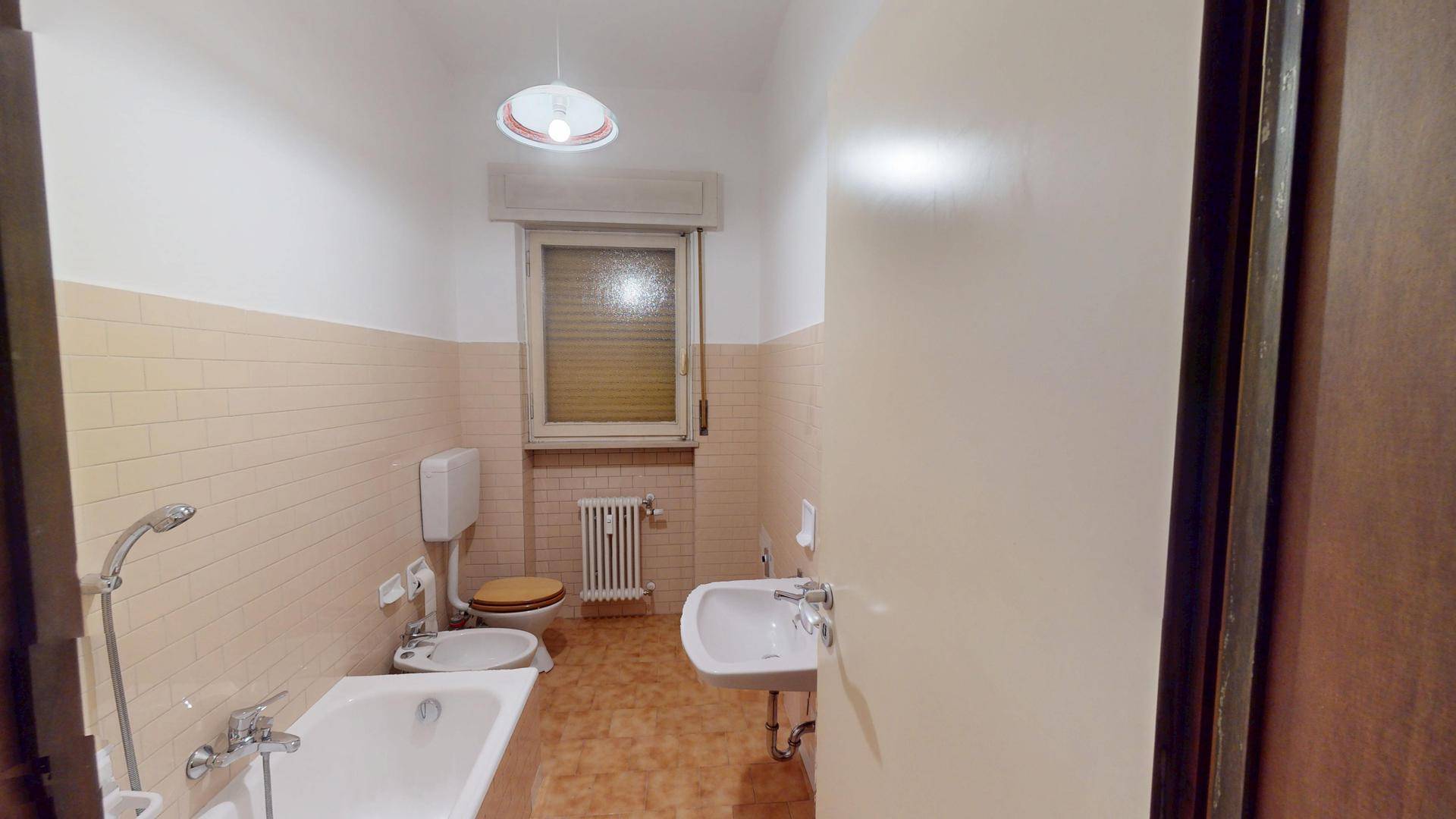 Badezimmer im 80er-Jahre-Stil mit Badewanne, Bidet, Waschbecken und Fenster.