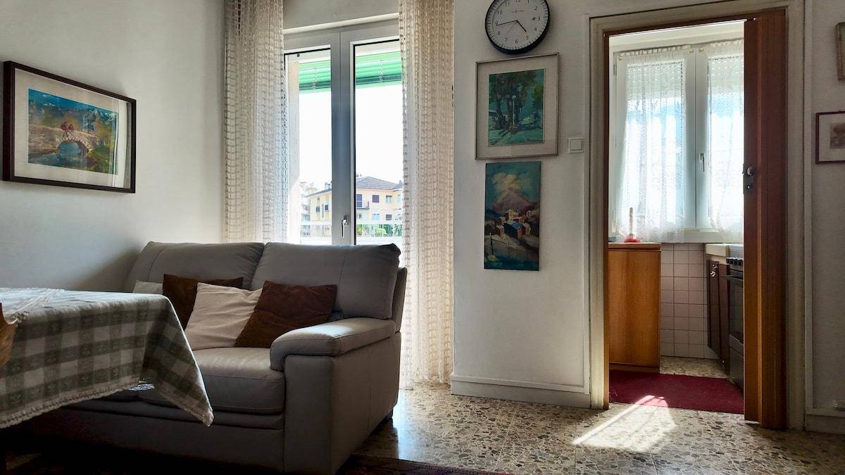 Gemütliches Wohnzimmer mit Sofa, Fenster und Blick in eine angrenzende Küche.