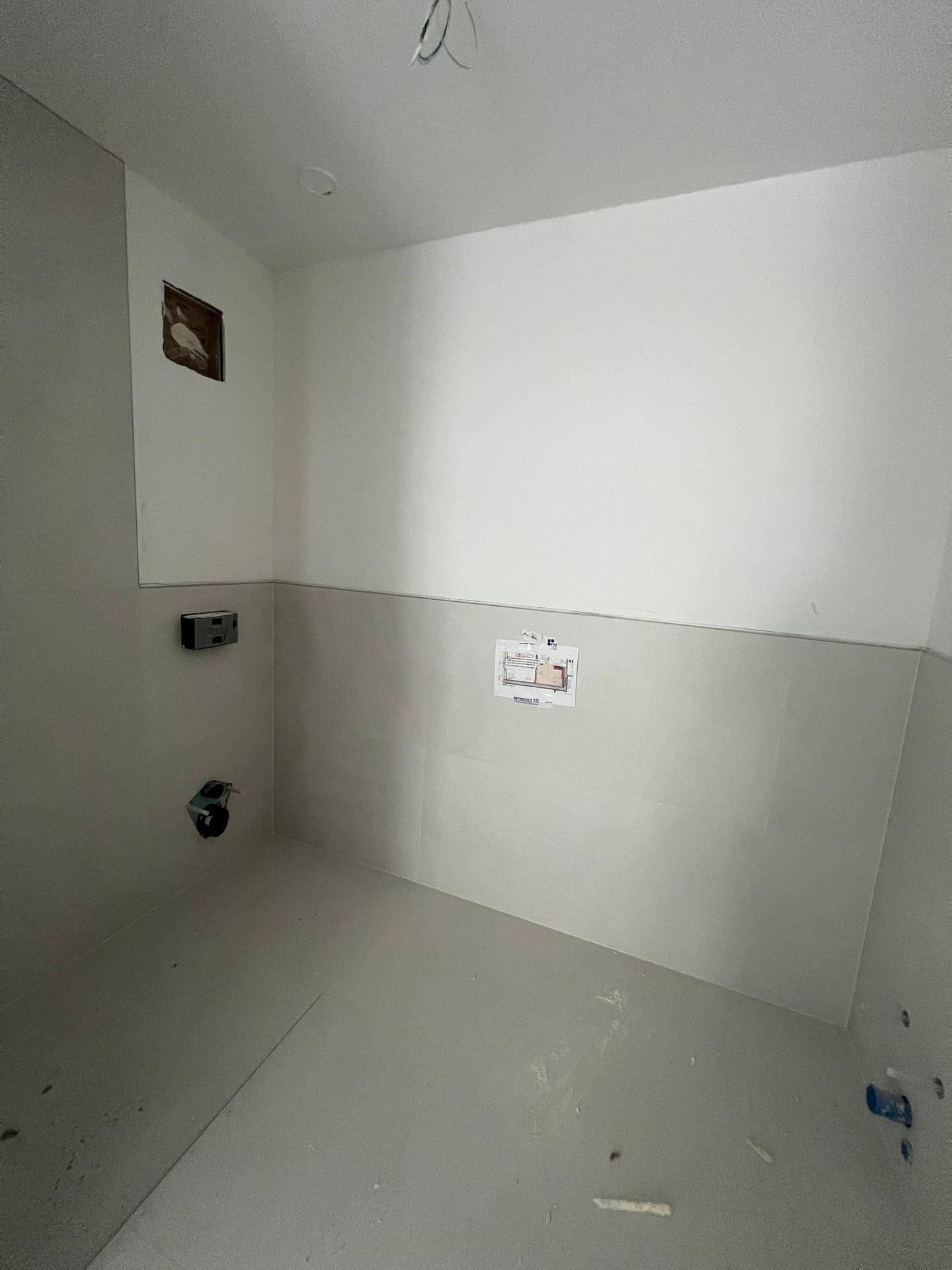 Unfertiges Badezimmer mit halbhohen Fliesen, weißen Wänden und sichtbaren Installationen.