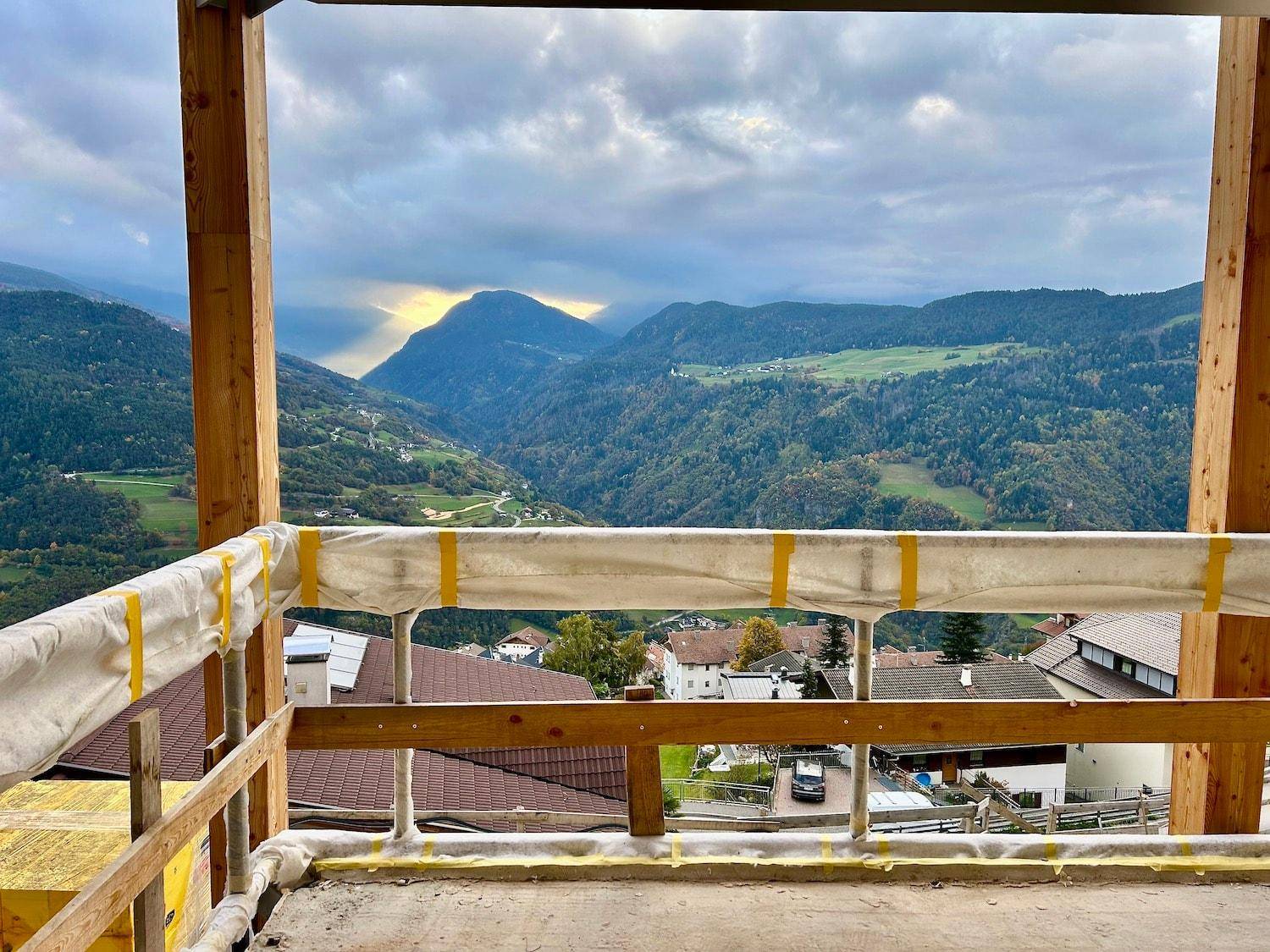 Aussicht von einem im Bau befindlichen Balkon mit Holzgeländer auf die beeindruckende Bergkulisse.