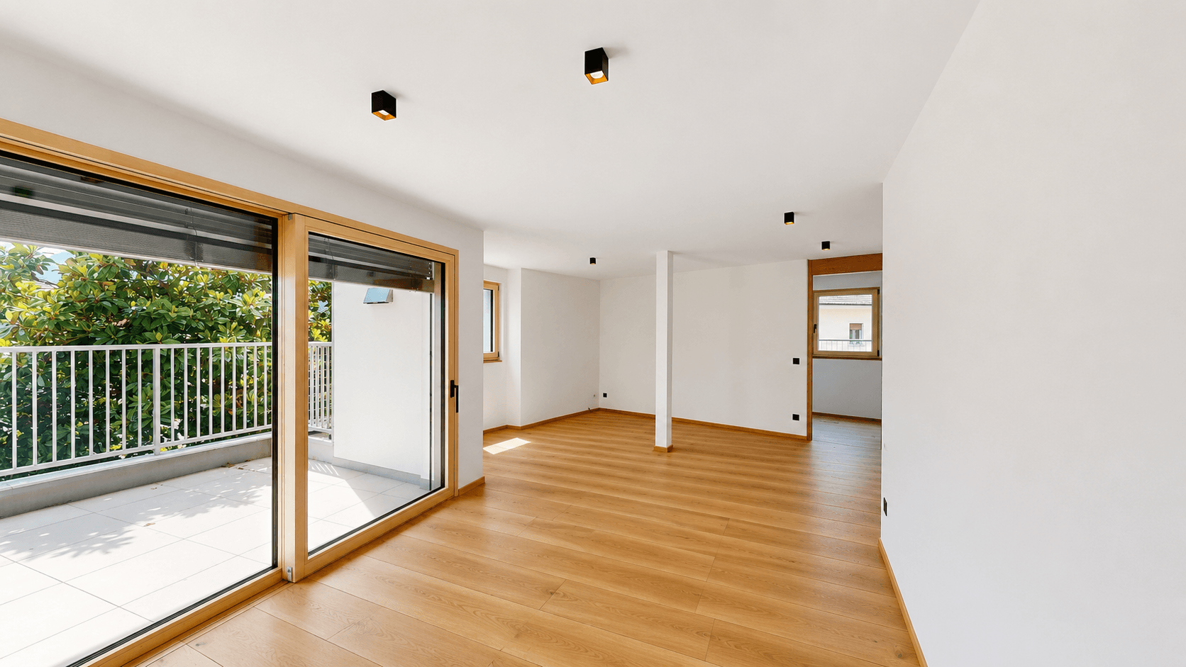Heller Wohnraum mit Holzboden und großem Balkonfenster, das viel Tageslicht hereinlässt.