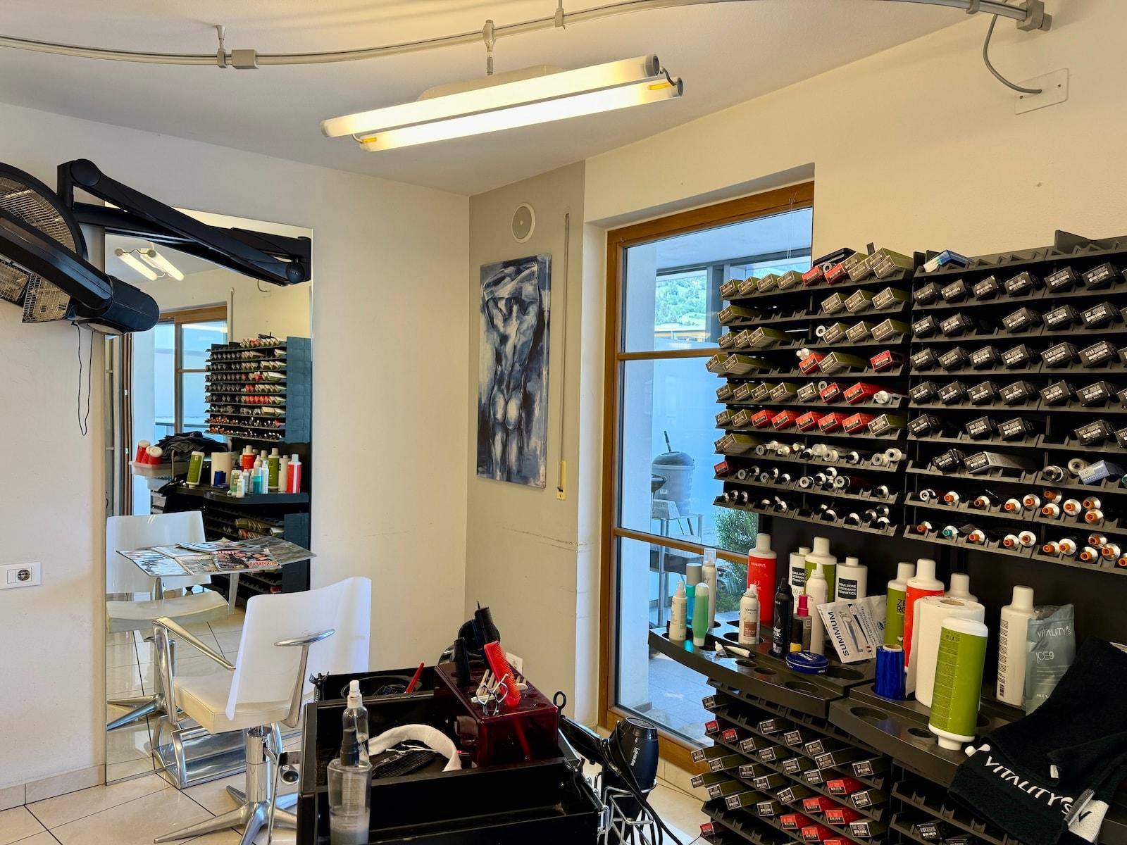 Friseursalon mit umfangreichen Produktregalen und einem Arbeitsplatz am Fenster.