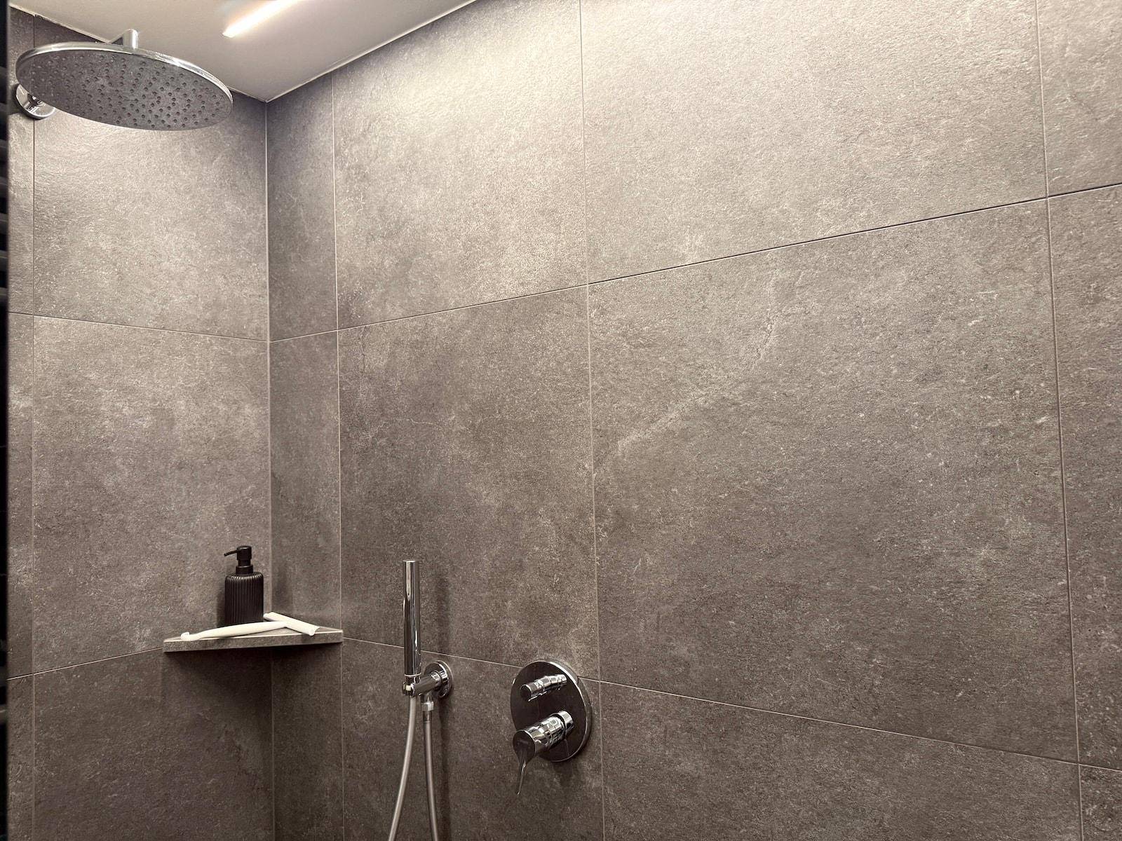 Nahaufnahme der modernen Dusche mit Regenduschkopf und eleganten grauen Wandfliesen.