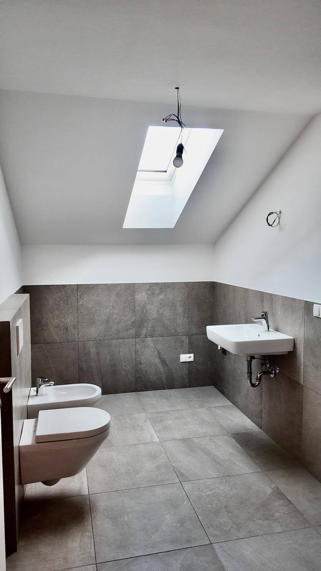 Modernes Badezimmer im Dachgeschoss mit Fliesenboden, Bidet und Dachfenster für Tageslicht.