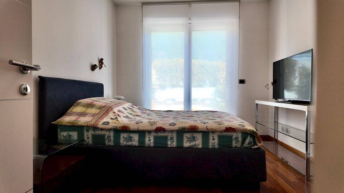Schlafzimmer mit Holzboden, Doppelbett und großem Fenster mit Blick ins Grüne.