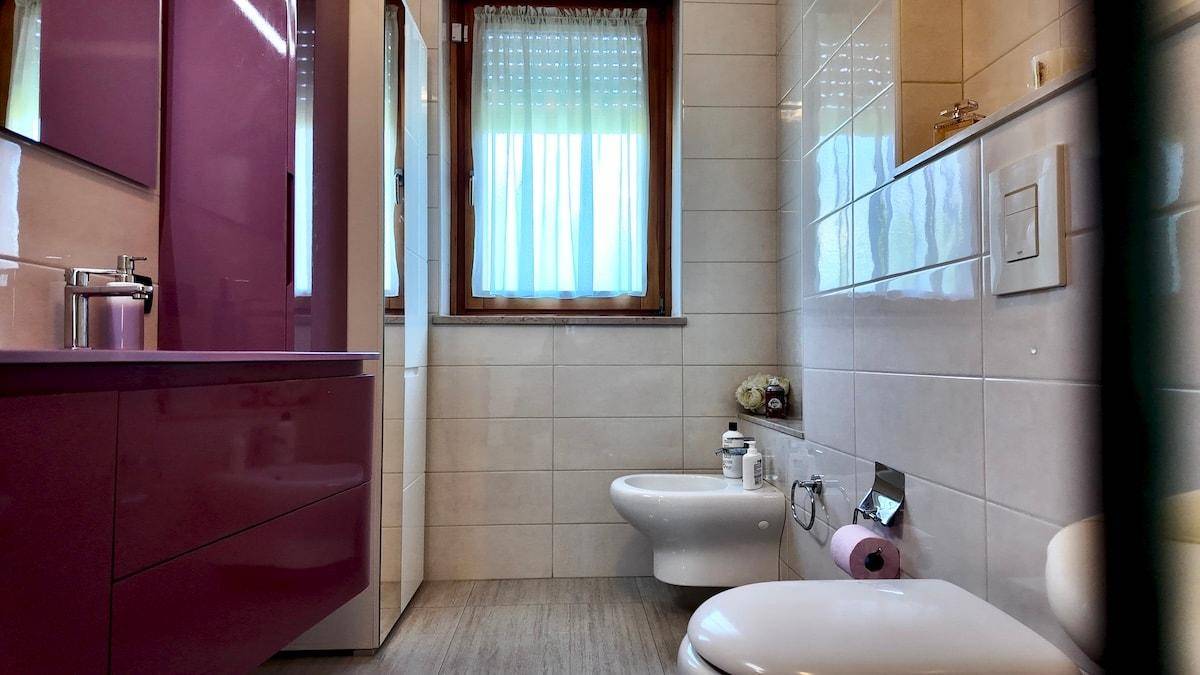 Modernes Badezimmer mit Bidet, WC, Fliesen und lila Waschtischunterschrank.