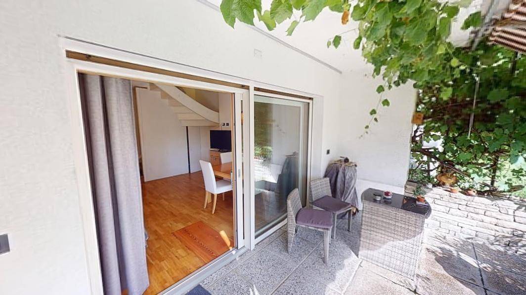 Blick von der Terrasse in den Garten, mit Sitzgelegenheiten und Zugang zum Innenbereich.
