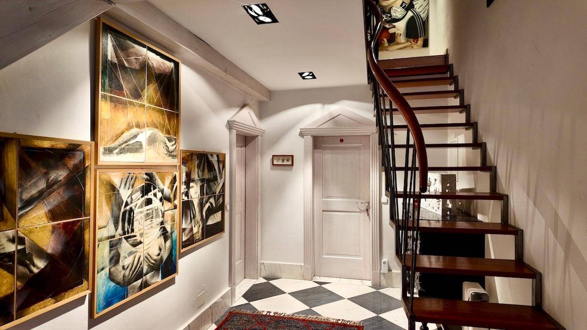Eleganter Flur mit geschwungener Holztreppe, schwarz-weißem Schachbrettboden und modernen Kunstwerken an den Wänden.