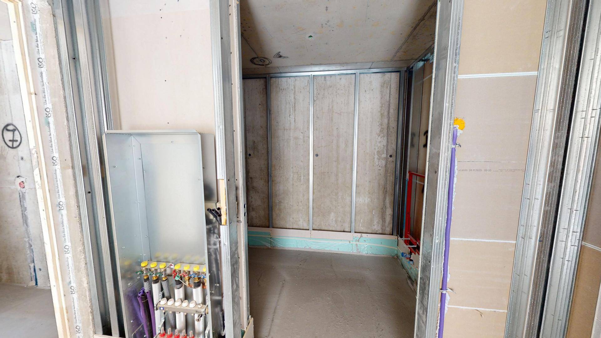 Innenraum im Rohbau mit Heizungsverteiler und vorbereiteten Wandstrukturen für den Ausbau.