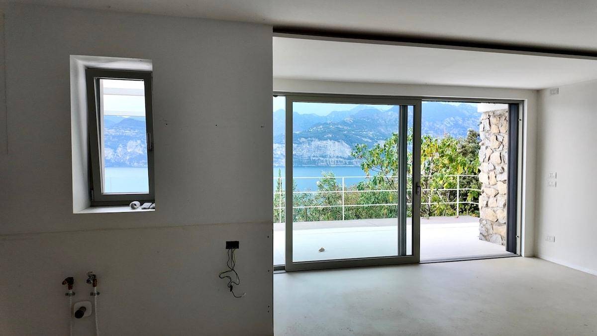 Leere Küche mit Betonboden und großen Glasschiebetüren, die einen weiten Blick auf den See bieten.