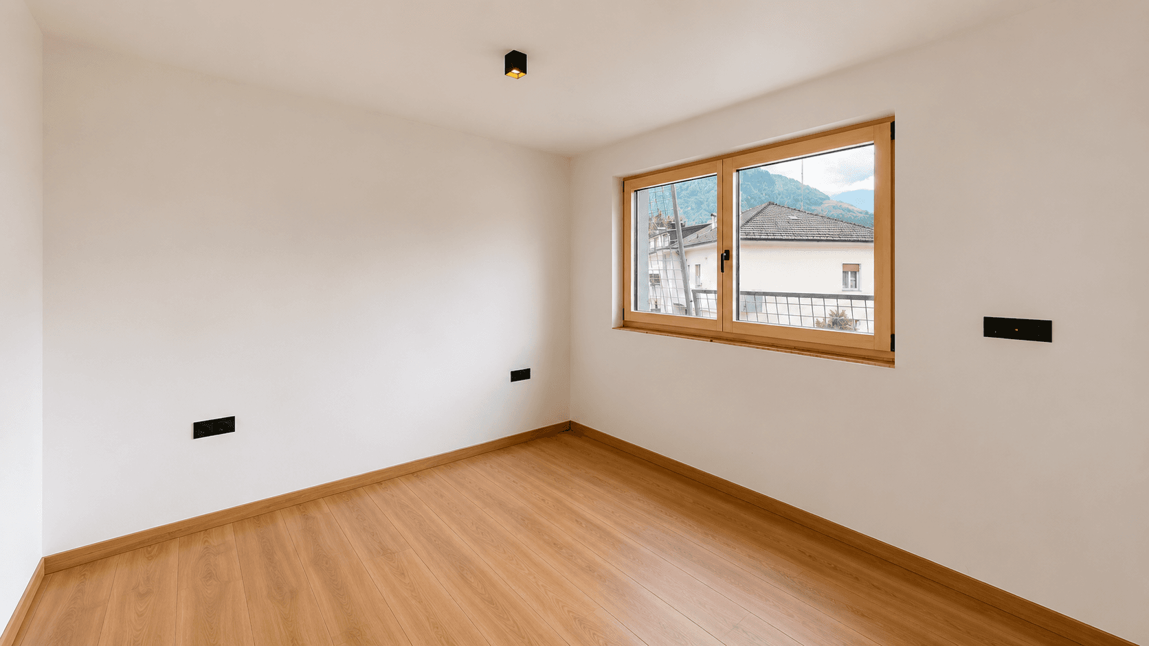 Helles Zimmer mit Holzboden und Fenster, das einen Blick auf die umliegende Landschaft bietet.