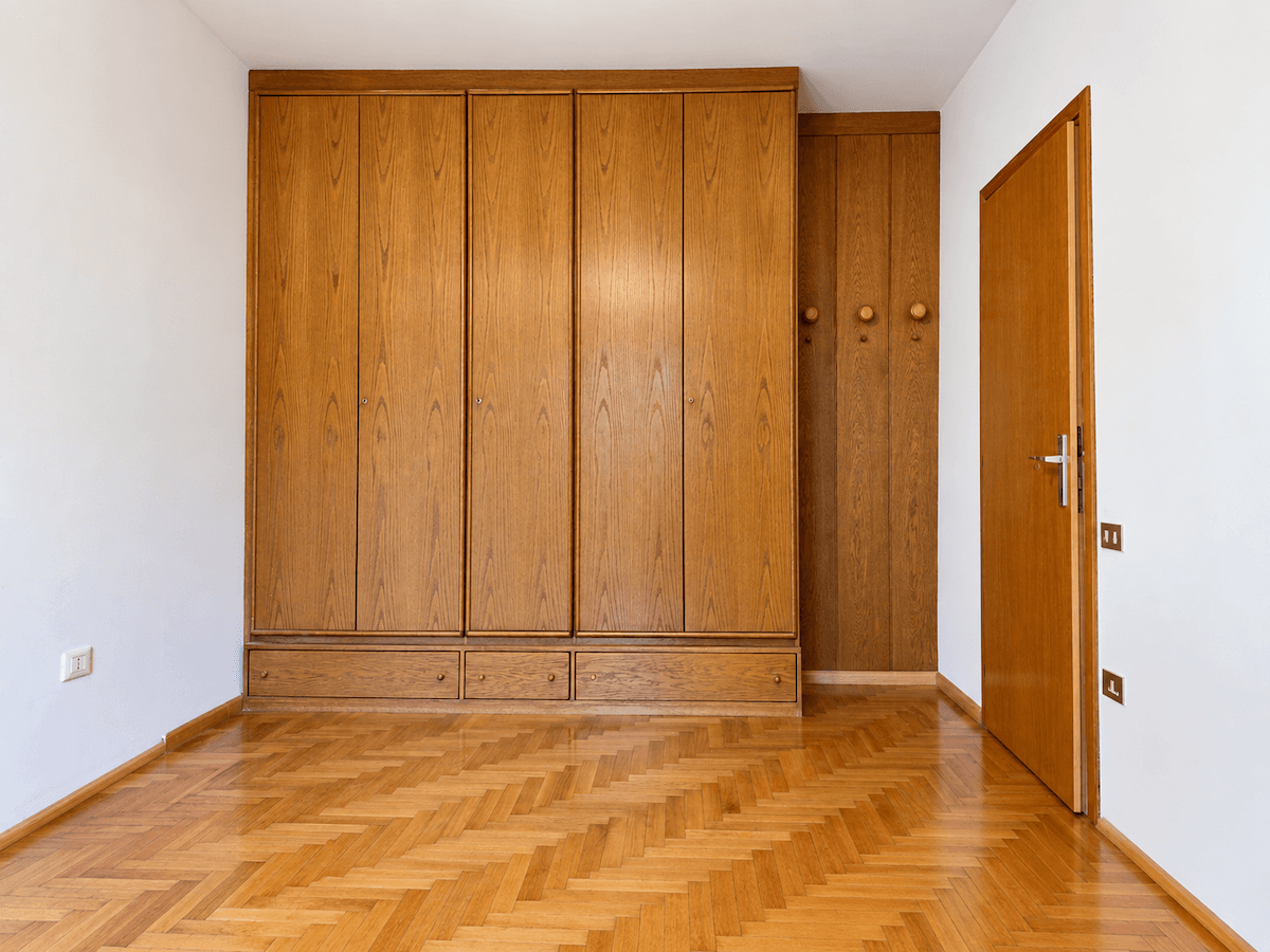 Leeres Schlafzimmer mit Fischgrätparkett und geräumigen Einbauschränken aus Holz.