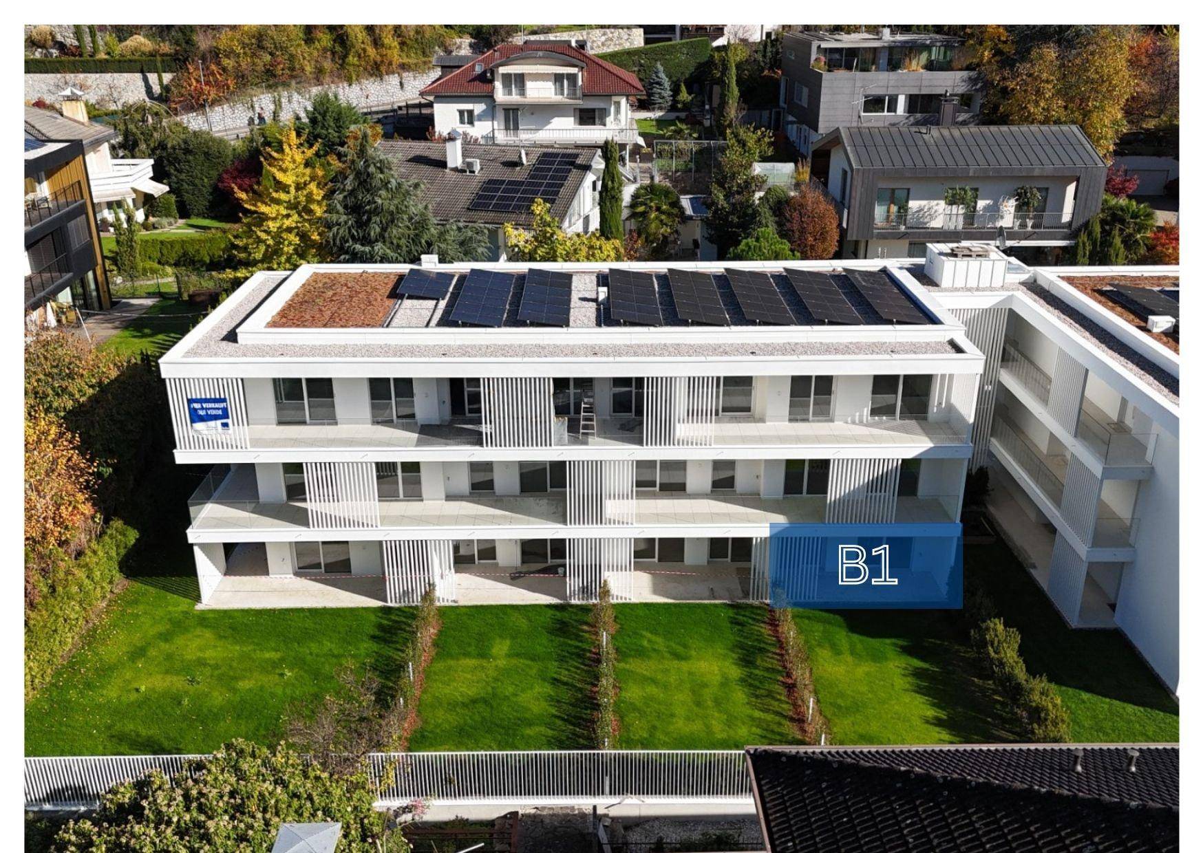 Moderne Wohnanlage mit klaren Linien, großzügigen Balkonen, Gründach und Photovoltaikanlage, eingebettet in eine grüne Umgebung.