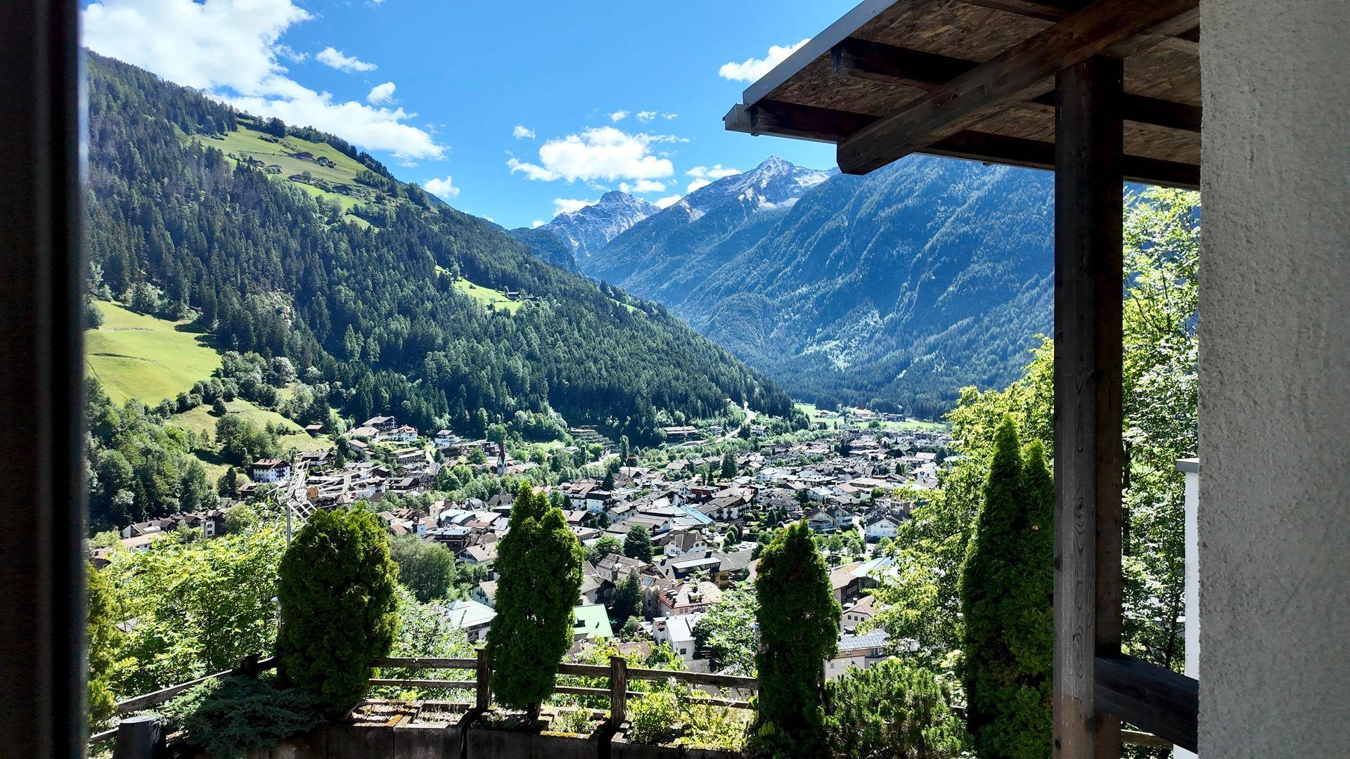 Panoramablick auf ein idyllisches Bergdorf und die umliegende Natur von einem überdachten Balkon.