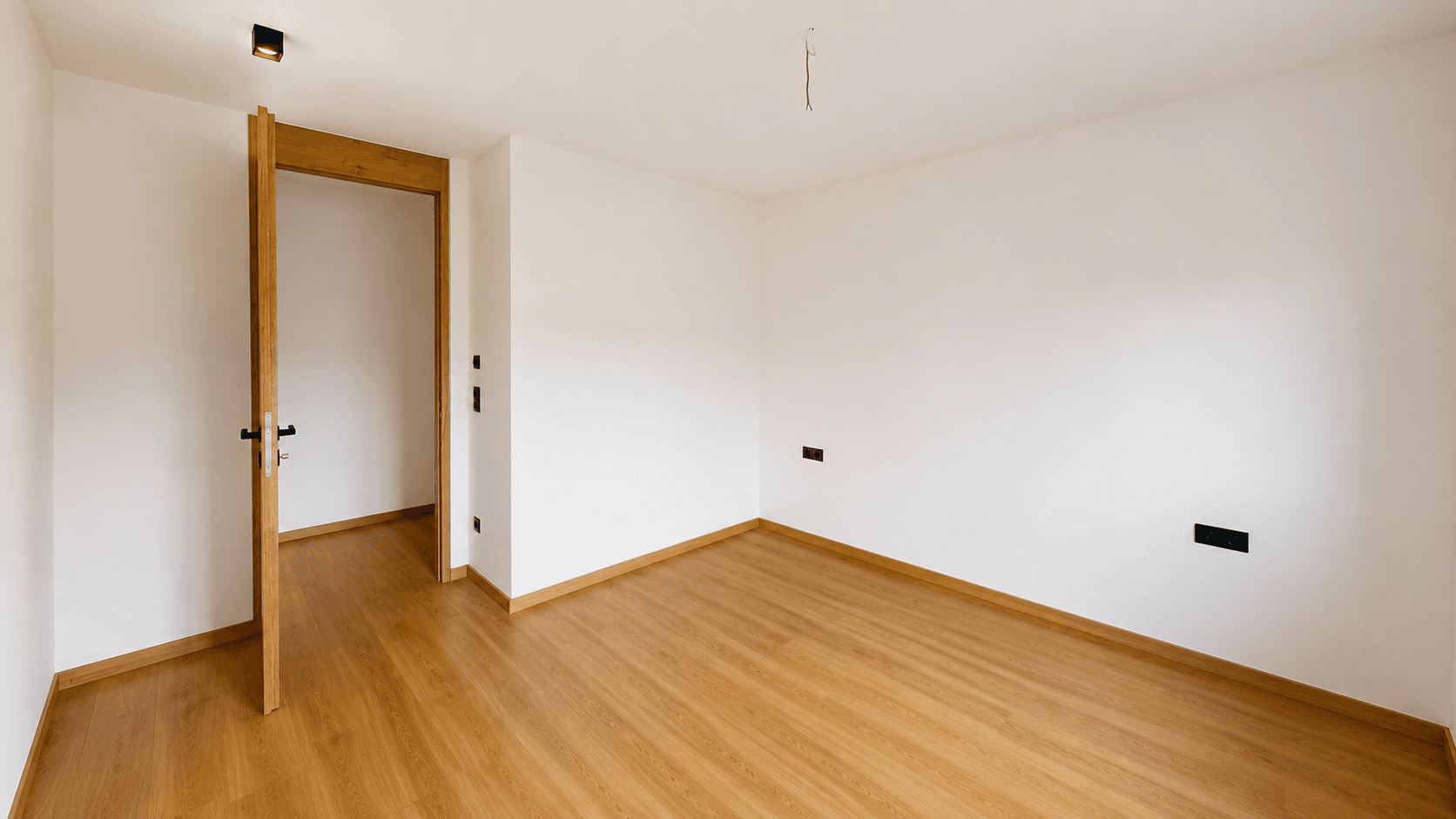 Geräumiges, helles Zimmer mit Holzboden und weiß gestrichenen Wänden.