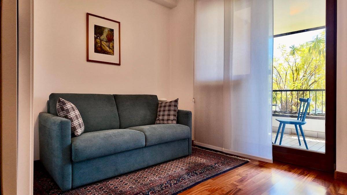 Wohnzimmer mit blauem Sofa, Holzboden und Zugang zu einem kleinen Balkon.
