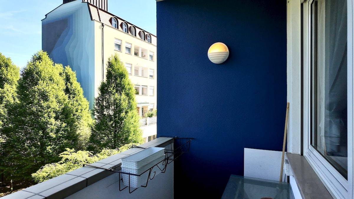 Balkon mit blauer Wand, Außenleuchte und Blick auf umliegende Gebäude.
