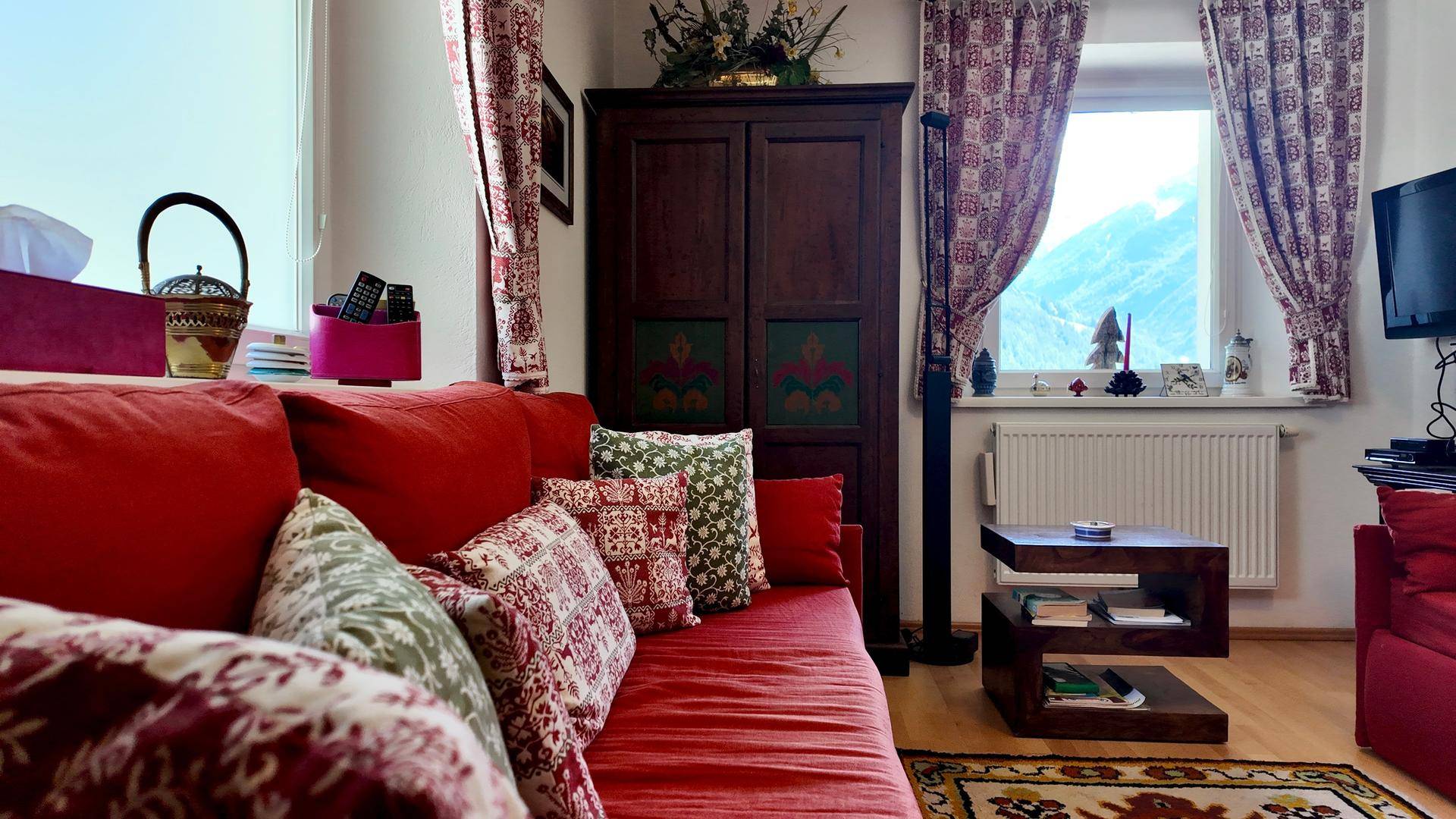 Gemütliches Wohnzimmer mit rotem Sofa, traditionellen Kissen und Blick auf die umliegenden Berge.